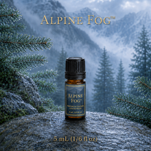 Alpine Fog™ perfume and cologne concentrate in an amber glass bottle with a blue-and-gold label, displayed against misty alpine mountains and wet silver fir branches - 5ml