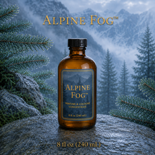 Alpine Fog™ perfume and cologne concentrate in an amber glass bottle with a blue-and-gold label, displayed against misty alpine mountains and wet silver fir branches - 8oz