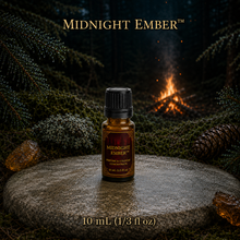 Midnight Ember™ perfume and cologne concentrate in an amber glass bottle with burgundy label beside a campfire in a dark evergreen forest -  10 ml