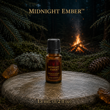 Midnight Ember™ perfume and cologne concentrate in an amber glass bottle with burgundy label beside a campfire in a dark evergreen forest -  15 ml