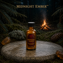 Midnight Ember™ perfume and cologne concentrate in an amber glass bottle with burgundy label beside a campfire in a dark evergreen forest -  2 fl oz
