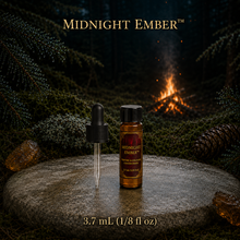 Midnight Ember™ perfume and cologne concentrate in an amber glass bottle with burgundy label beside a campfire in a dark evergreen forest -  Dram, 3.7ml